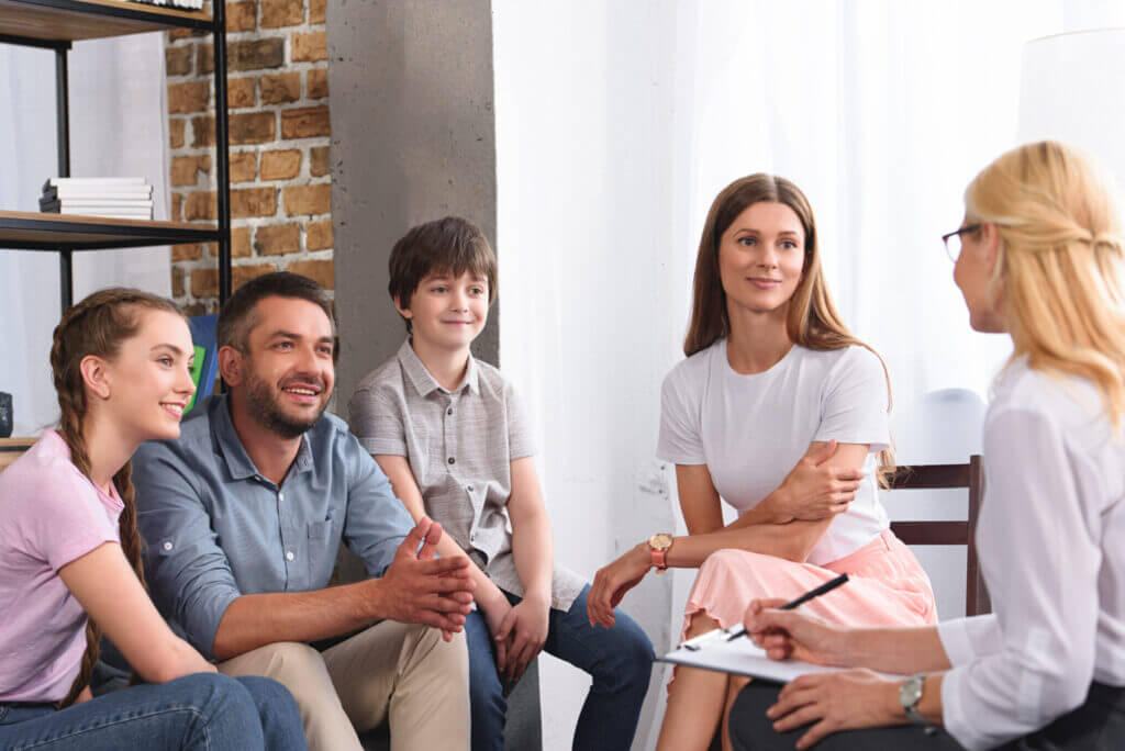 Happy family sitting on therapy session by female counselor writing in clipboard in office